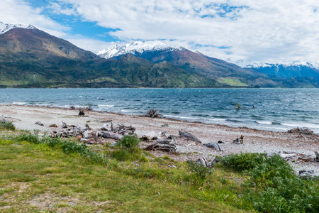 On a windy day the lake is wild with waves crashing into the shore. The mountains of the region maintain their snow at its peaks while white clouds form above.の写真素材