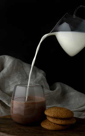Milk is poured into a glass with cacao from a transparent jug and oat cookiesの写真素材
