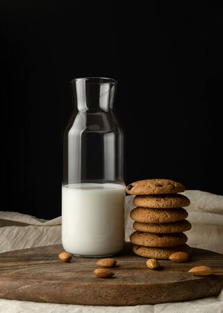 Oat cookies with pieces of chocolate, almond, milk in a glass bottle on cutting board on white textileの写真素材