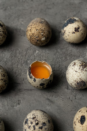 Several quail eggs on a concrete surface. One egg is broken and the yolk is visible in center frame...