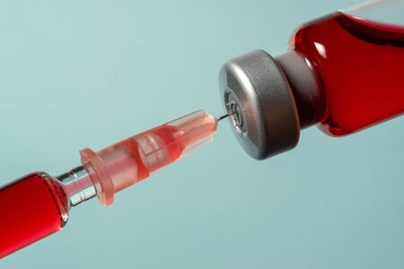 Needle pierces the cap of medical vial with red liquidの写真素材