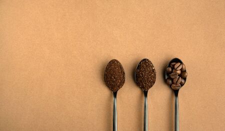 Different grinding coffee, coffee beans, coarse coffee, finely ground coffee in black metal spoons. Top view on brown background.の写真素材