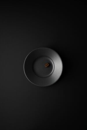 One coffee bean in black saucer on a black surface in the center of the frame. Flat lay.の写真素材