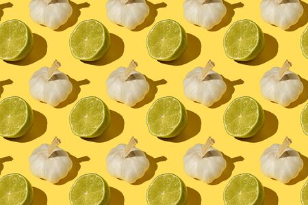 Lime halves and bulbs of garlic on a yellow background with hard light, colorful bright pattern, close-up.の写真素材
