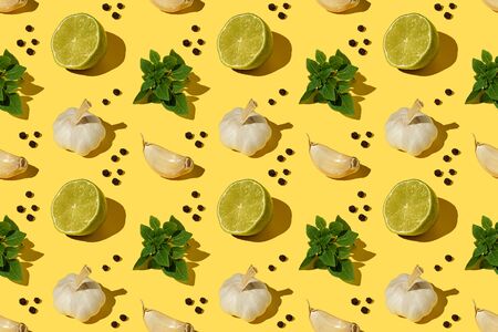 Basil leaves, garlic bulbs, halves of lime, cloves of garlic, peppercorns on a yellow backgroundの写真素材