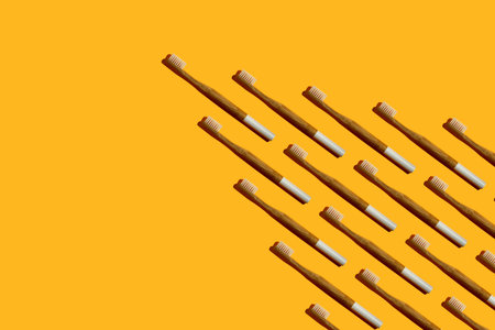 Wedge or arrow shaped bamboo toothbrushes with a white handle and hard shadow on yellow background....