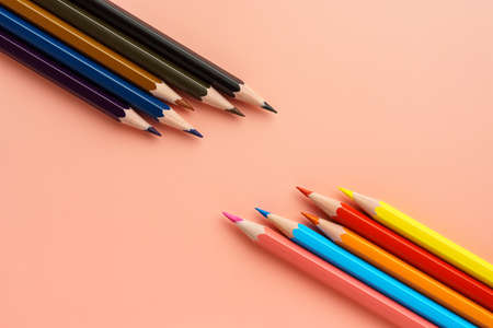 Colored bright pencils lie opposite dark pencils on pink backgroundの写真素材