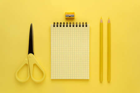 Notepad, yellow pencil and yellow scissors on a yellow backgroundの写真素材