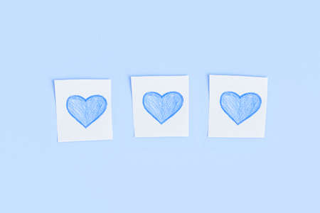 Three blue hearts drawn in pencil on pieces of white paperの写真素材
