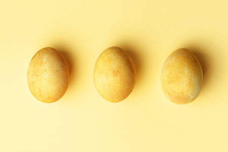 Three Easter golden eggs in a row on a yellow background