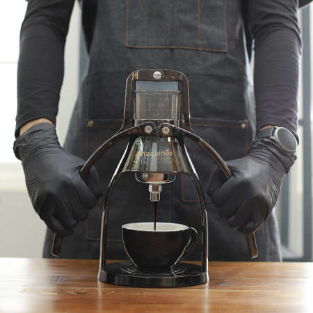 Barista standing behind Coffee Machine Manual, demonstrating how to press the coffee beans into the black cup.の写真素材
