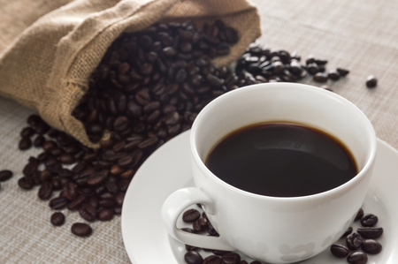 black coffee in a white cup and coffee beans in hemp sack on naperyの写真素材