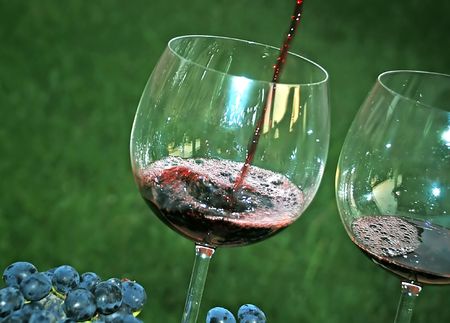 pour red wine in glass over green backgroundの写真素材