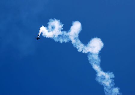 small plane in acrobatic flight with spiral trace over blue skyの写真素材