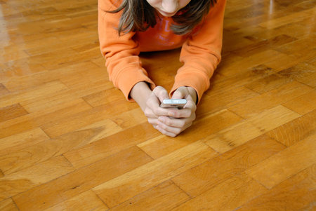 Teen girl lying on wooden parquet floor with mobile phone