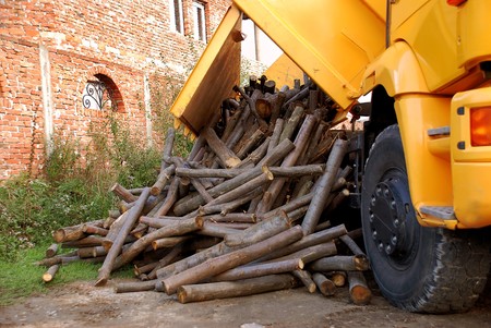 unloading wood delivery from yellow truck by brick houseの写真素材