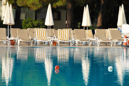 empty chairs with sunshades by blue swimming pool in summer resort