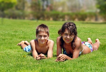 smiling boy and girl lying on green grass outdoors at summerの写真素材