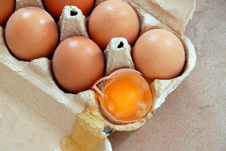 brown eggs in cardboard box, one broken egg closeup