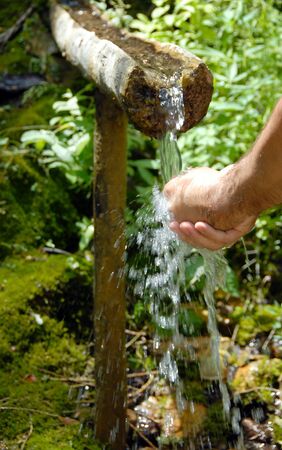 man washing his hands by spring water under wooden gutter over green natural backgroundの写真素材
