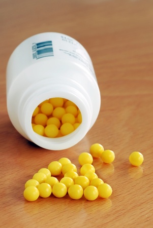 yellow vitamin pills scattered from white plastic bottleの写真素材