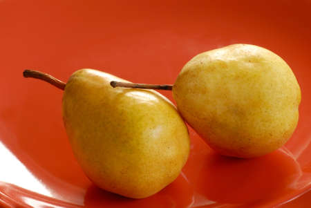 two appetizing yellow pears on red plateの写真素材