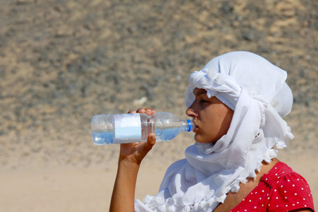 teen girl tourist drinking water in egyptian kerchief in desertの写真素材