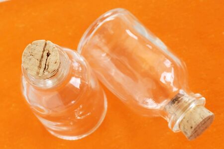 two small empty glass bottles closed with corks over orange backgroundの写真素材
