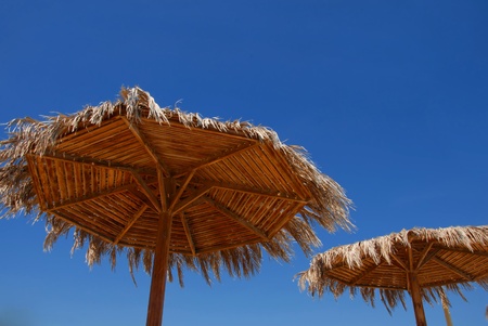 two straw wooden sunshades over blue sky on beach at resortの写真素材