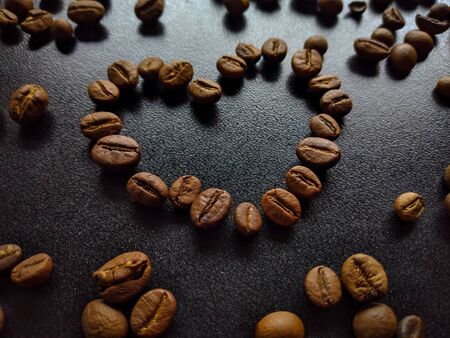 Selective focus of roasted coffee beans. Coffee beans in heart shape on black rustic wooden background, love of coffee, symbol of love.の写真素材