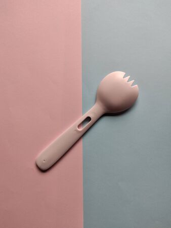 Pink spoon and fork plastic isolated on two colors background. Plastic cutlery, kitchen utensil, serving set. Kitchenware.の写真素材