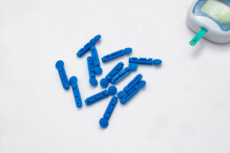 A set of blue lancets or needles for diabetic glucose blood sugar monitoring. A glucometer can be partially seen with a strip plugged in for a reading.の写真素材