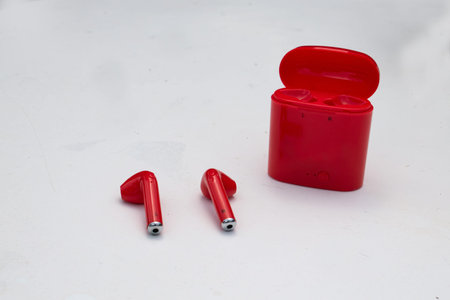 A pair of of bright red, wireless earbuds or headphones isolated on a gray background with a...