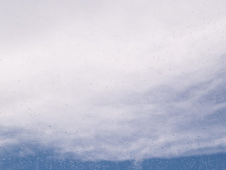 Rain drops on window looking out at blue sky with clouds.の写真素材
