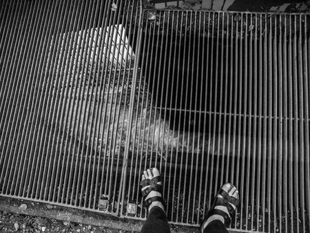 Looking down at feet in black leather sandals standing on grate over rushing water.