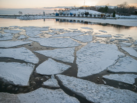 Covered boats on Lake Ontario with floating ice chunks and snow, in Oakville, Ontario, Canada in...