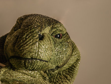 Green head of lizard costume staring down at camera against a beige background.
