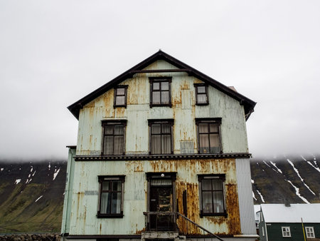 Rusty green house on a street in front of a low lying cloud and snow striped mountain in Isafjordur...