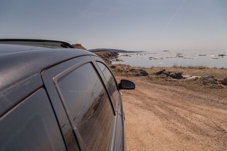 A black car stopped at the side of a dirt road along the Cabot Trail in Nova Scotia, east coast Canada, in the springtime. Chunks of ice and snow float in the Atlantic ocean.の写真素材