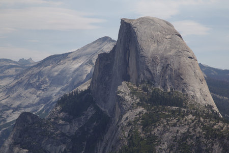 View of Half Dome from Glacier Point in Yosemite National Park. The sky is blue with a haze and soft...