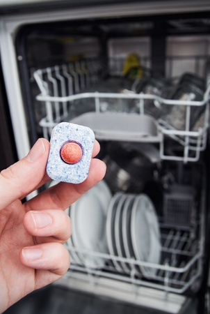 Hand holding dishwashing tablet. Dishwasher in backgroundの写真素材