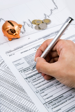 Man hand filling PIT-11 income tax forms with piggybank and coinsの写真素材