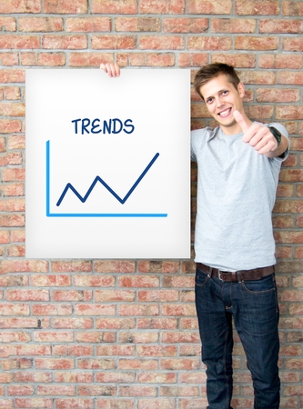 Young man holding whiteboard with trends chartの写真素材