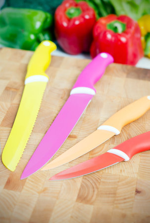 Ceramic knifes on a chopping board. Fresh vegetables in background