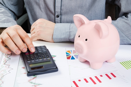 Man calculates money. Piggy bank and business documents on desk Man calculates money. Piggy bank and business documents on desk