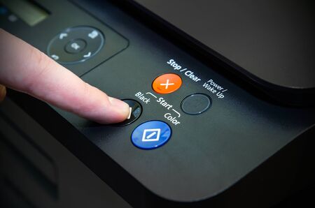 Man holding finger on start button of laser printerの写真素材