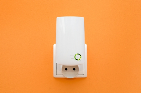 WiFi repeater in electrical socket on orange wall. Simply way to extend wireless network in homeの写真素材