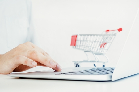 Man using laptop for internet shopping. Bright composition with shopping trolley in background.の写真素材
