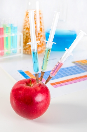 Three syringes in red apple. Genetically modified food in lab concept.の写真素材