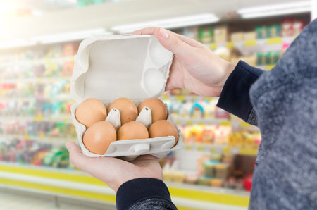 Man holding egg box in supermarket. egg box buy carton man hold checking consumer conceptの写真素材